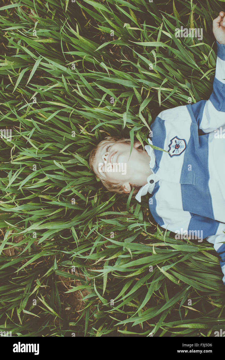 Cute little boy lying in long grass smiling Stock Photo