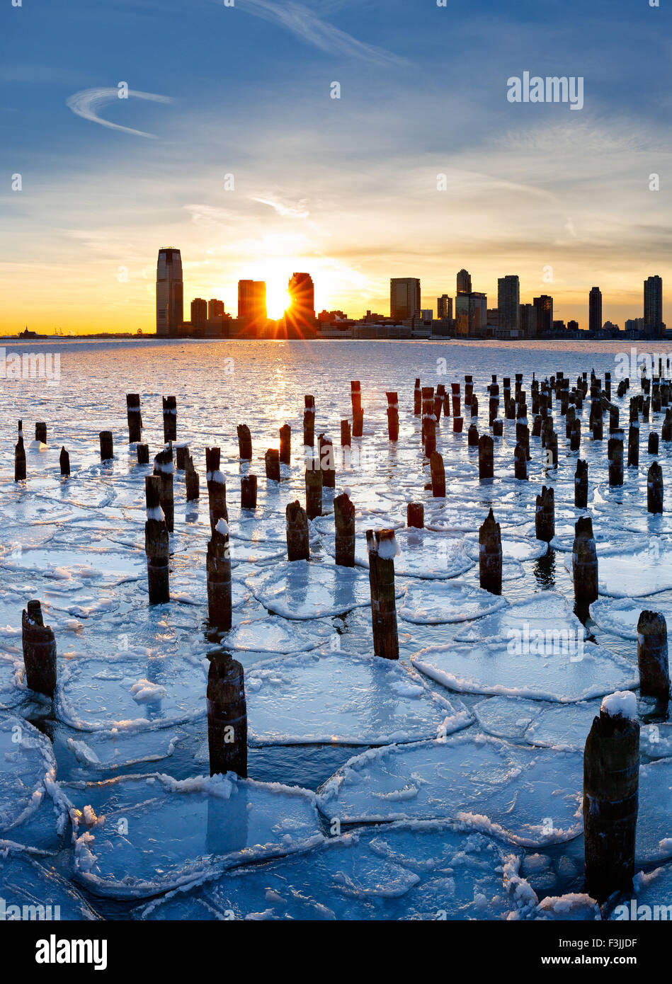 Wood pilings from New York old pier sticking out through the ice on Hudson River at sunset with Jersey City buildings Stock Photo