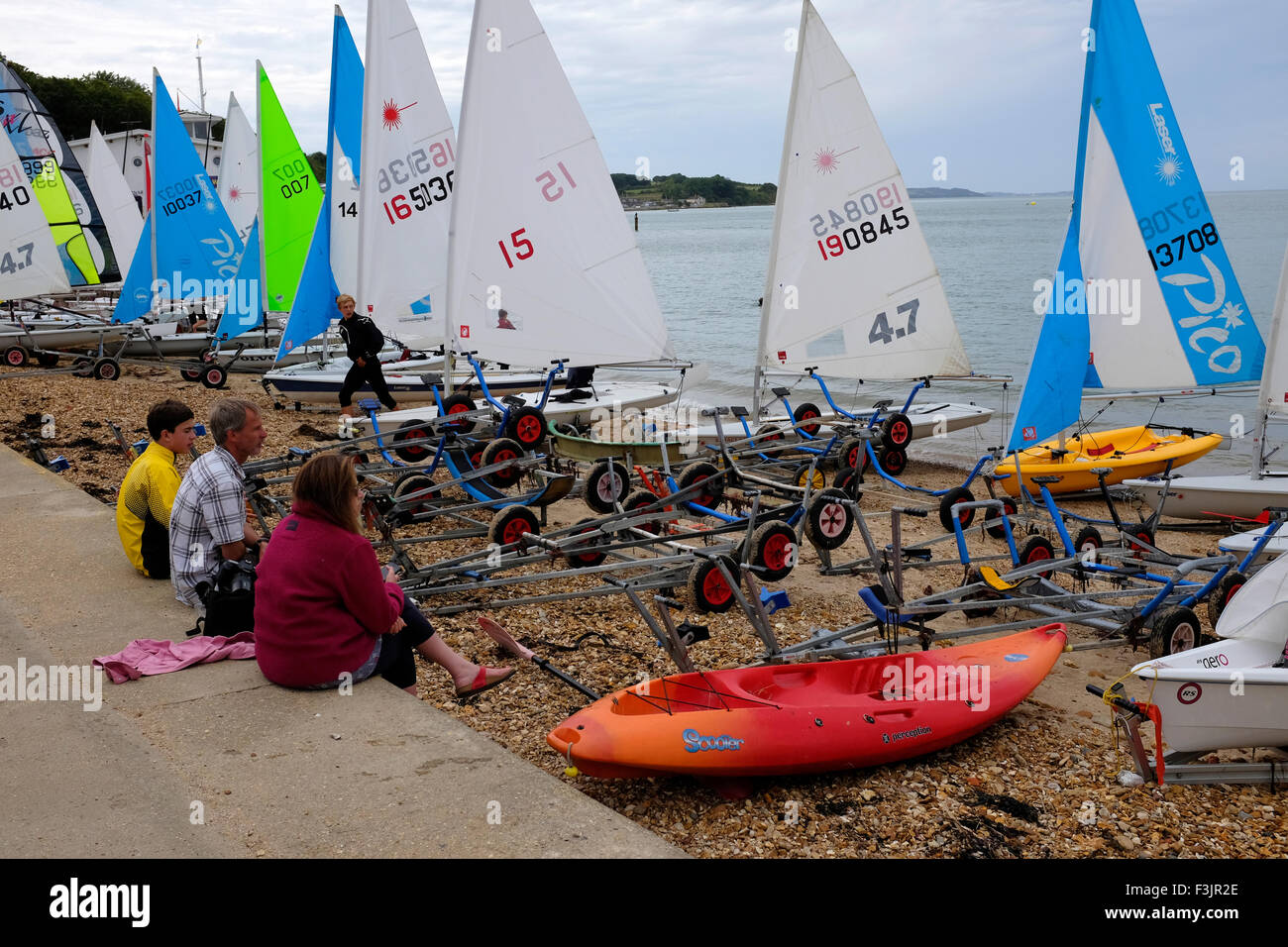 People sat on beach watching dinghy sailors preparing for Gurnard Dinghy Week Cowes Isle of Wight England UK Stock Photo