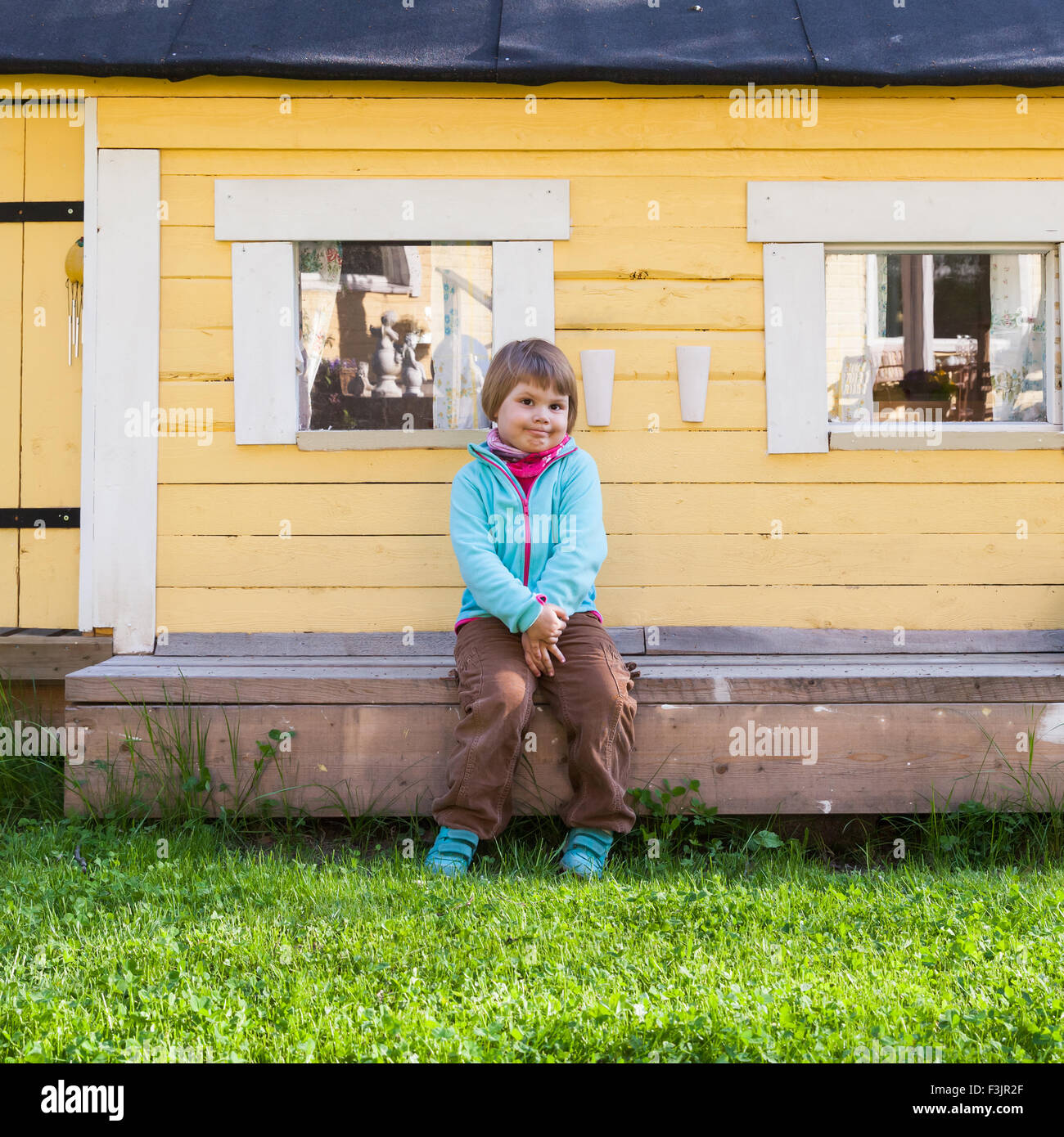 Outdoor portrait of cute Caucasian blond girl near small rural wooden ...