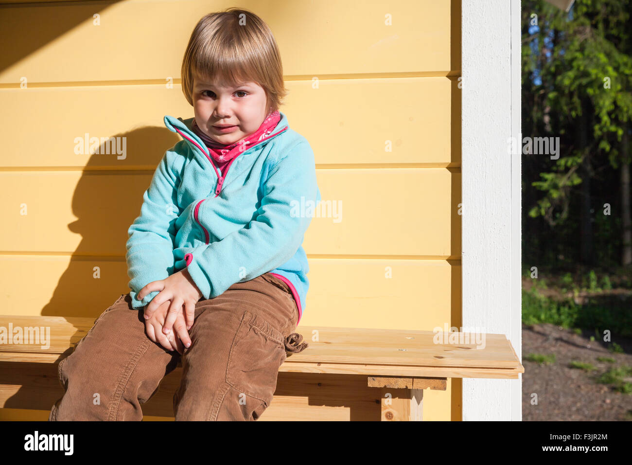 Outdoor portrait of confused Caucasian blond girl near rural wooden house wall Stock Photo