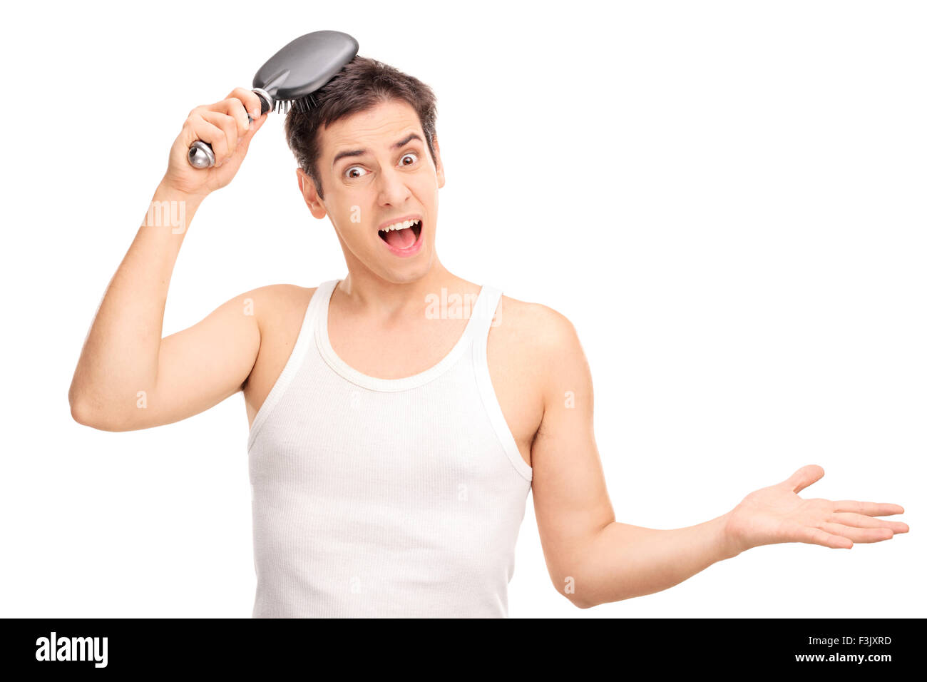 Angry young man brushing his hair with a hairbrush and looking at the camera isolated on white background Stock Photo