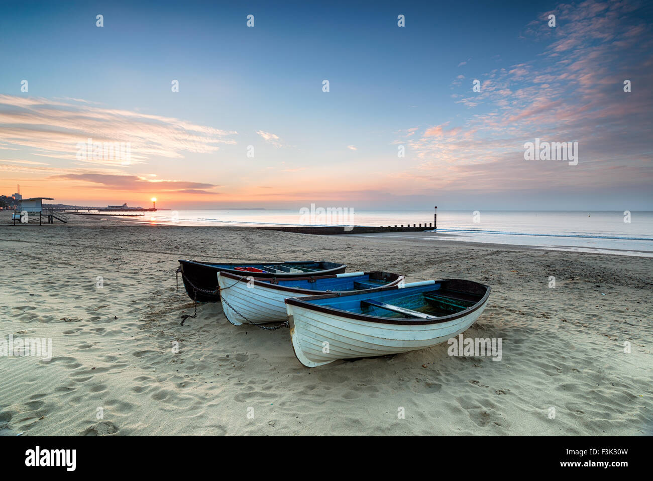 Stunning sunrise over a row of fishing boats on Bournemouth beach in Dorset, with the pier in