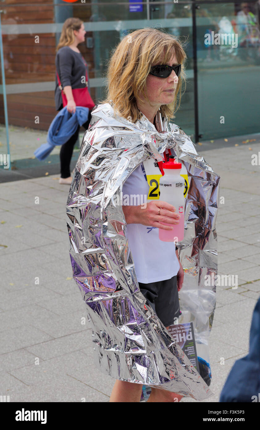 Woman half marathon competitor cools down in thermal silver wrap while recovering after finish, Bristol 2015 run Stock Photo