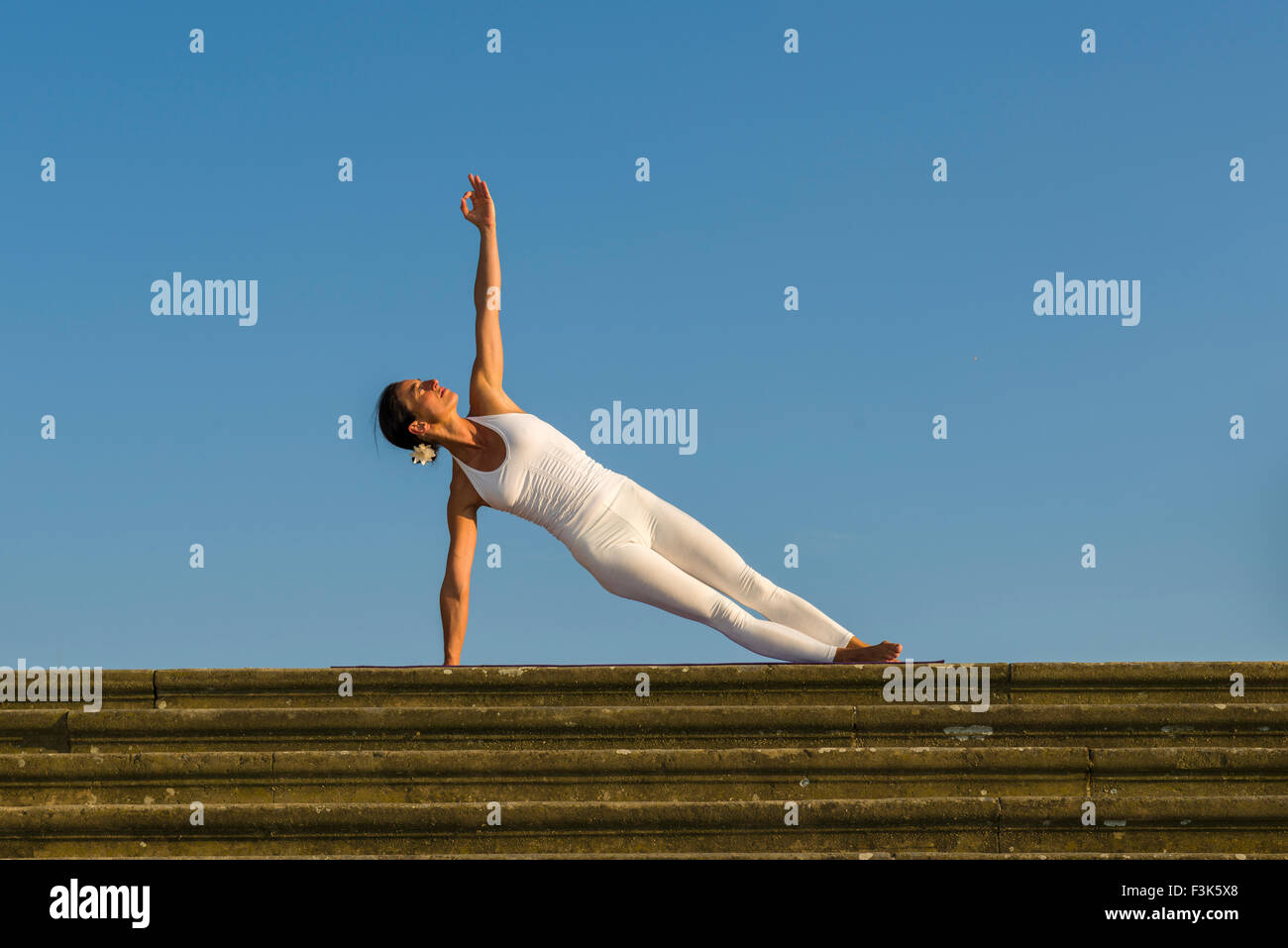 Young woman, wearing a white body suit, is practising Hatha-Yoga outdoor, showing the pose: vasishthasana, sage vashishta's pose Stock Photo