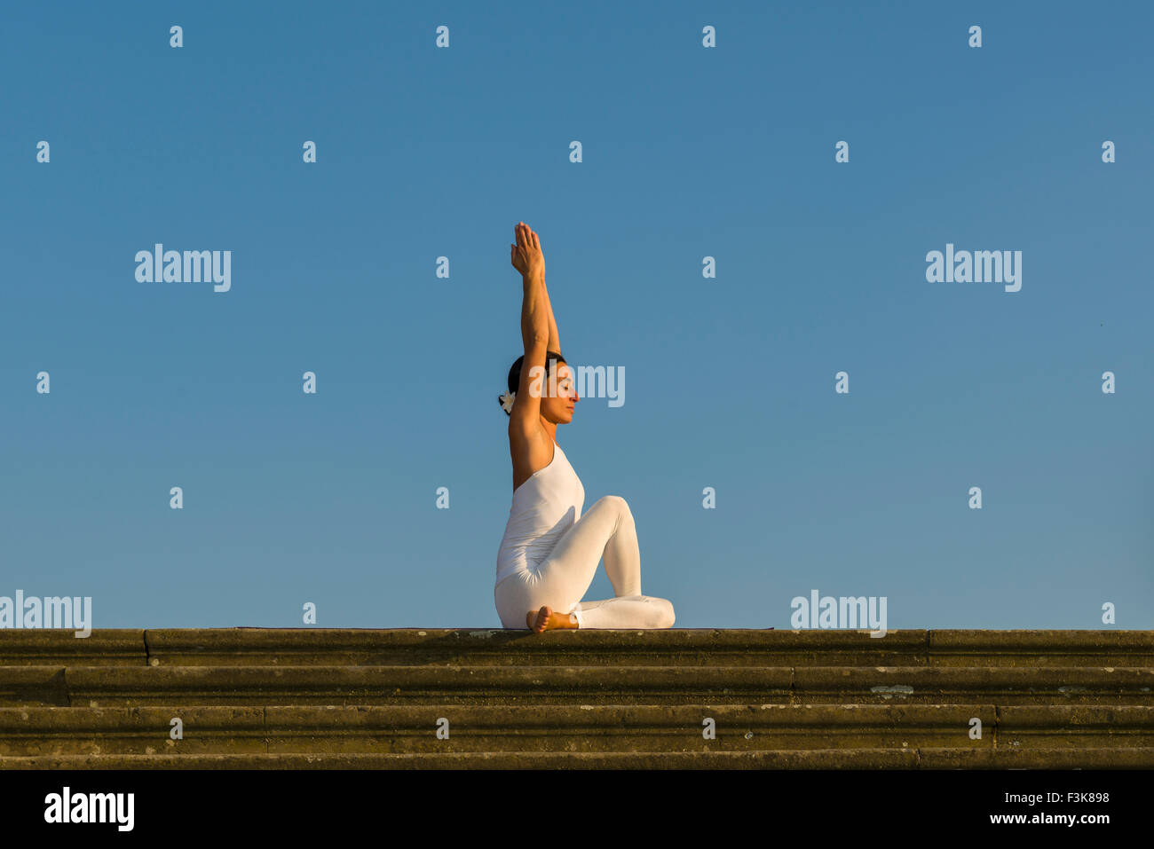 Young woman, wearing a white body suit, is practising Hatha-Yoga outdoor, showing the pose: ardha matsyendrasana, half spinal tw Stock Photo