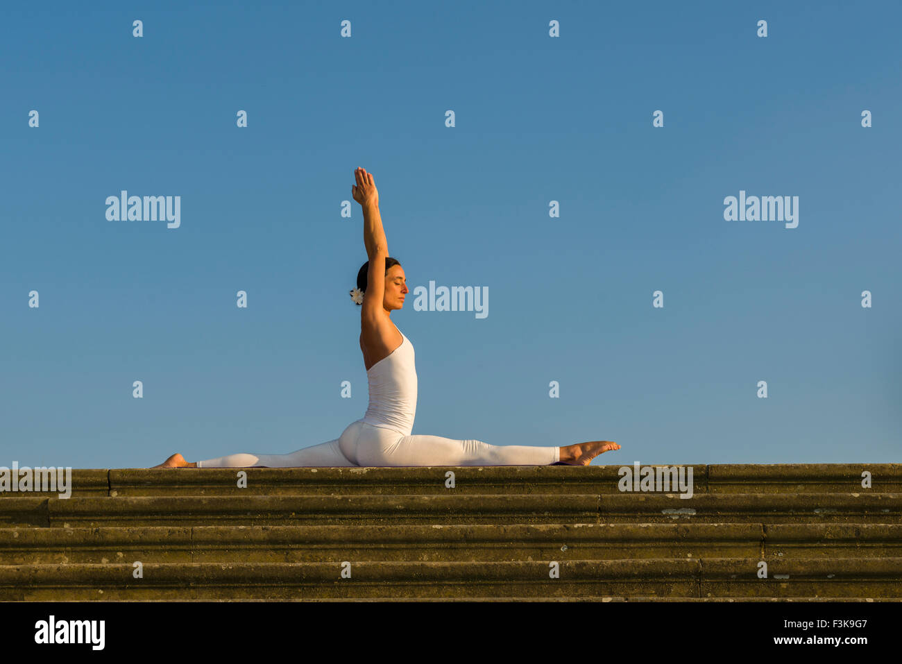 Supple young woman athlete doing a yoga frontal split stretch on a