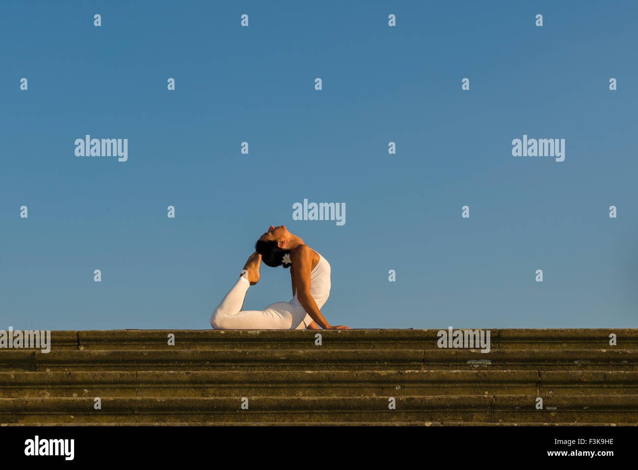 Young woman, wearing a white body suit, is practising Hatha-Yoga outdoor, showing the pose: bhujangasana, cobra pose Stock Photo