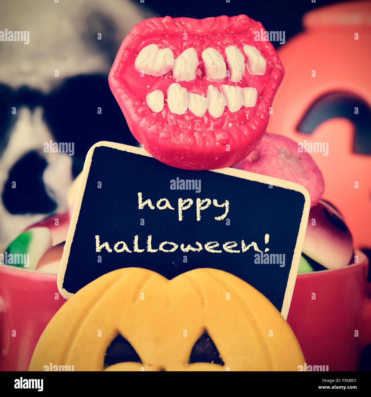 the text happy halloween written in a chalkboard, different candies and cookies, and some scary ornaments, such as a skull or a Stock Photo