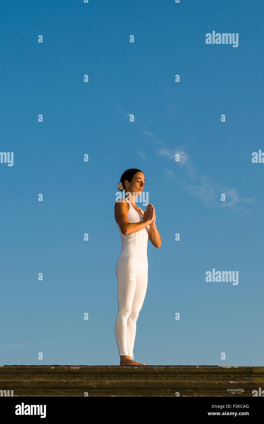 Young woman, wearing a white body suit, is practising Hatha-Yoga outdoor, showing the pose: tadasana / pranamasana, prayer pose Stock Photo