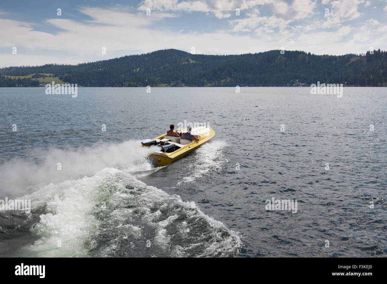 Two men in a yellow speedboat heading out into a lake on a sunny summer day. Stock Photo