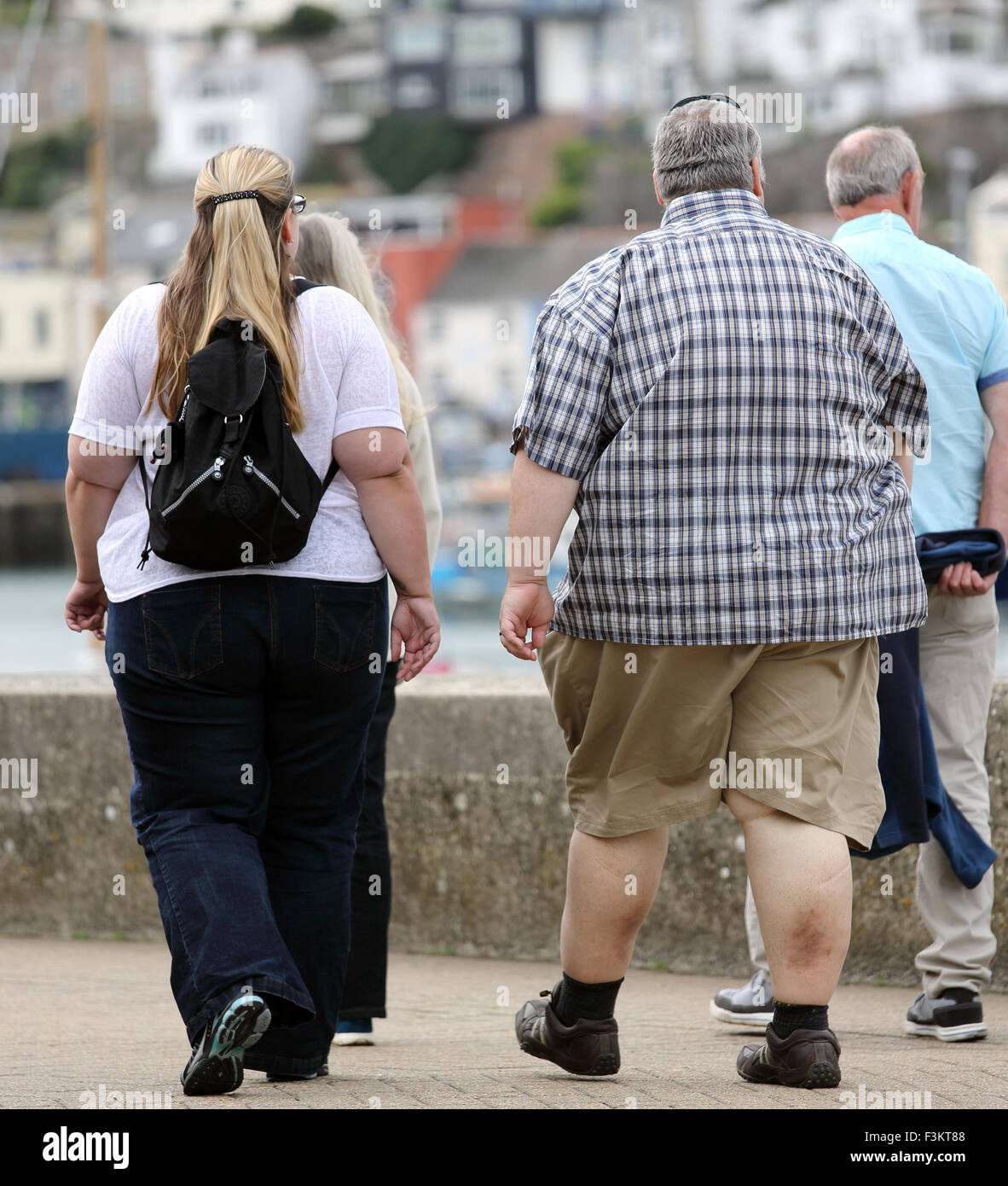 An obese couple walk alongside the harbour in Brixham, Devon, England, UK Stock Photo