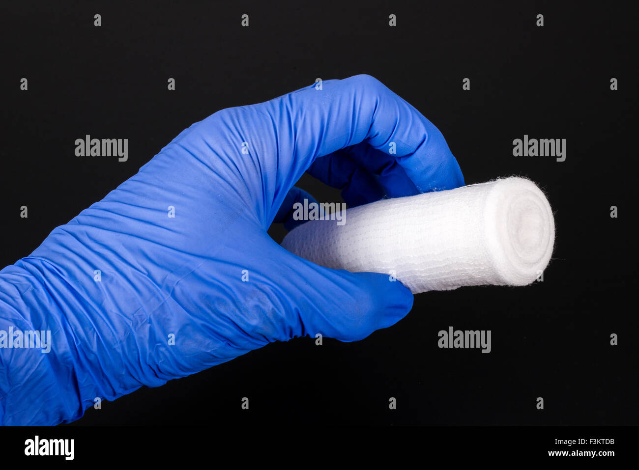 A hand in a blue medical glove is holding a white gauze bandage for medical use, displayed on a