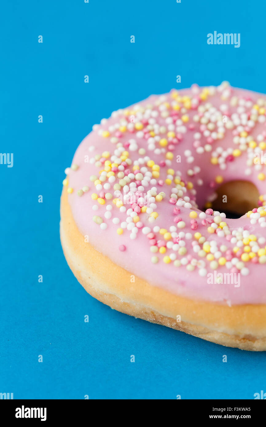 donut with pink frosting and sprinkles on turquoise Stock Photo