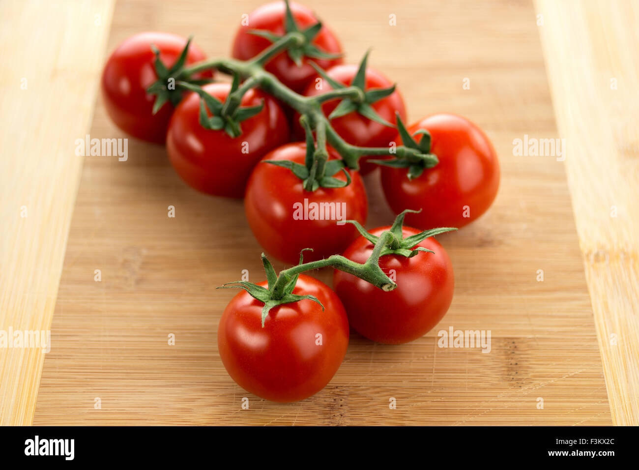 Red ripe cherry tomatoes with vines on a wooden cutting board. Macro view with shallow depth of field. Stock Photo