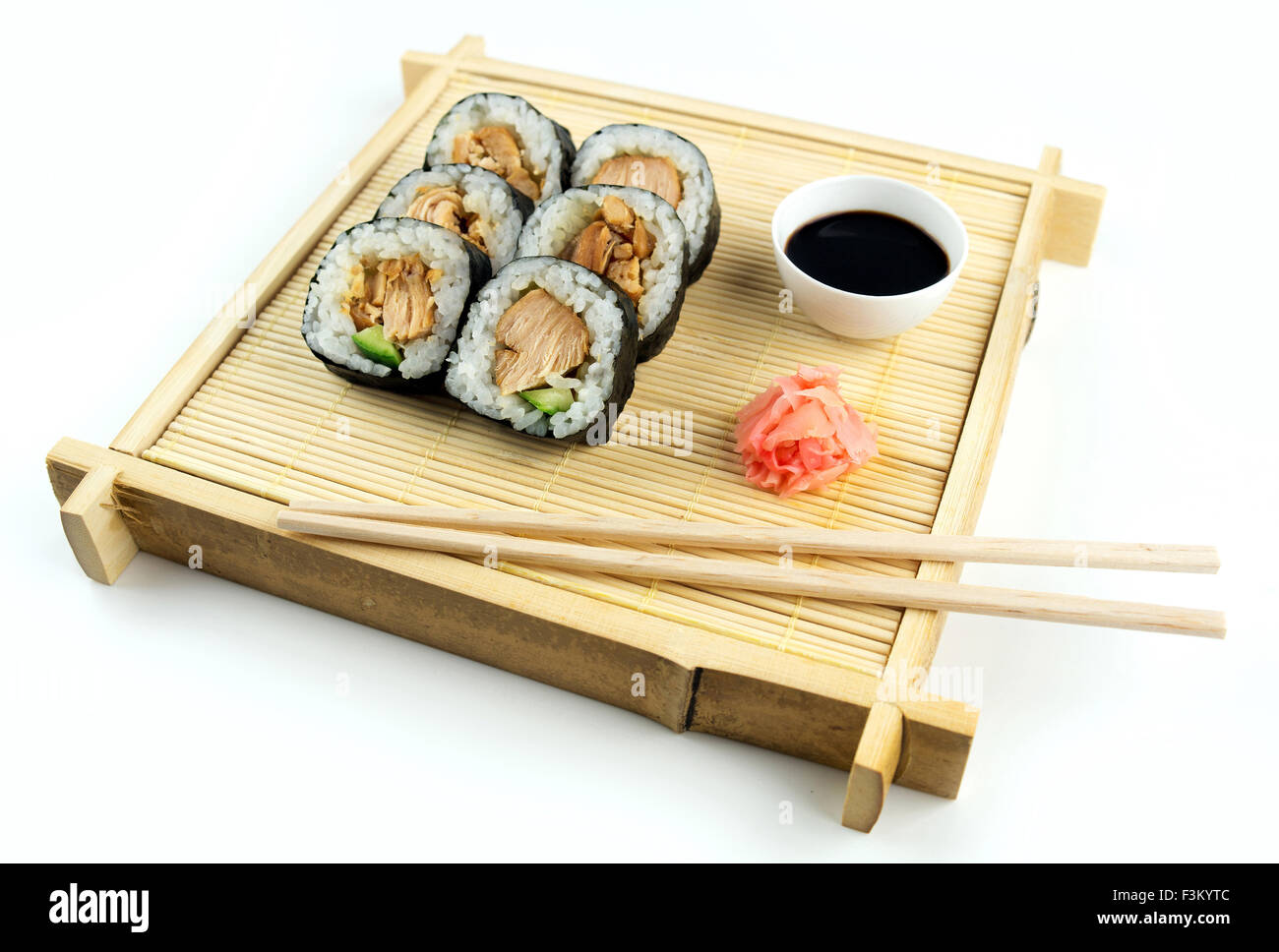 Old fashioned Japanese setting with teriyaki sushi, chopsticks and condiments on a bamboo tray and mat Stock Photo