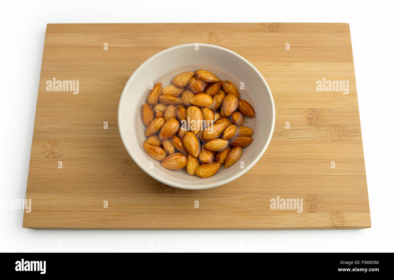 Almonds with water in a bowl against a wooden board, isolated on a white background Stock Photo