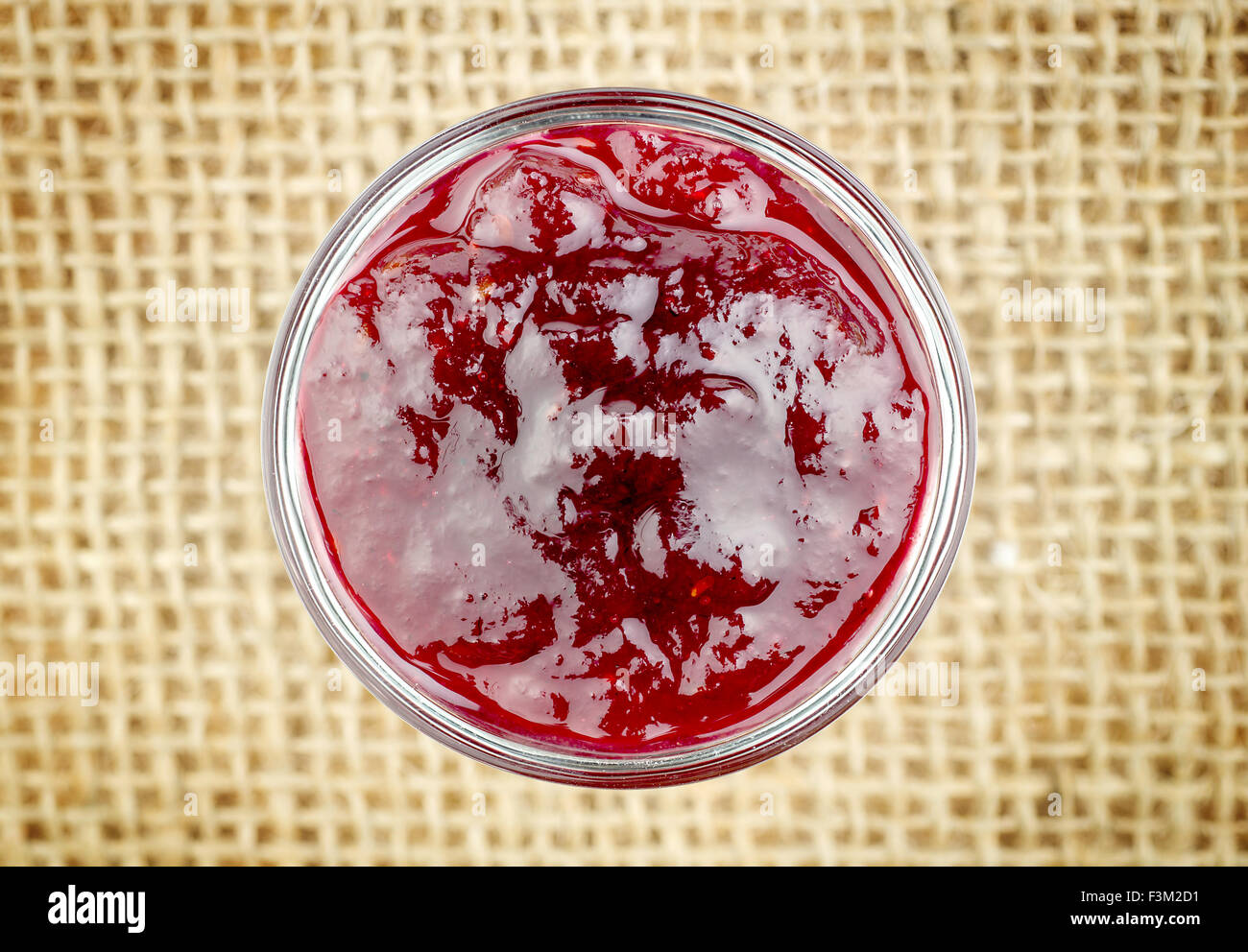 Aerial shot of strawberry jam against rustic burlap background Stock Photo