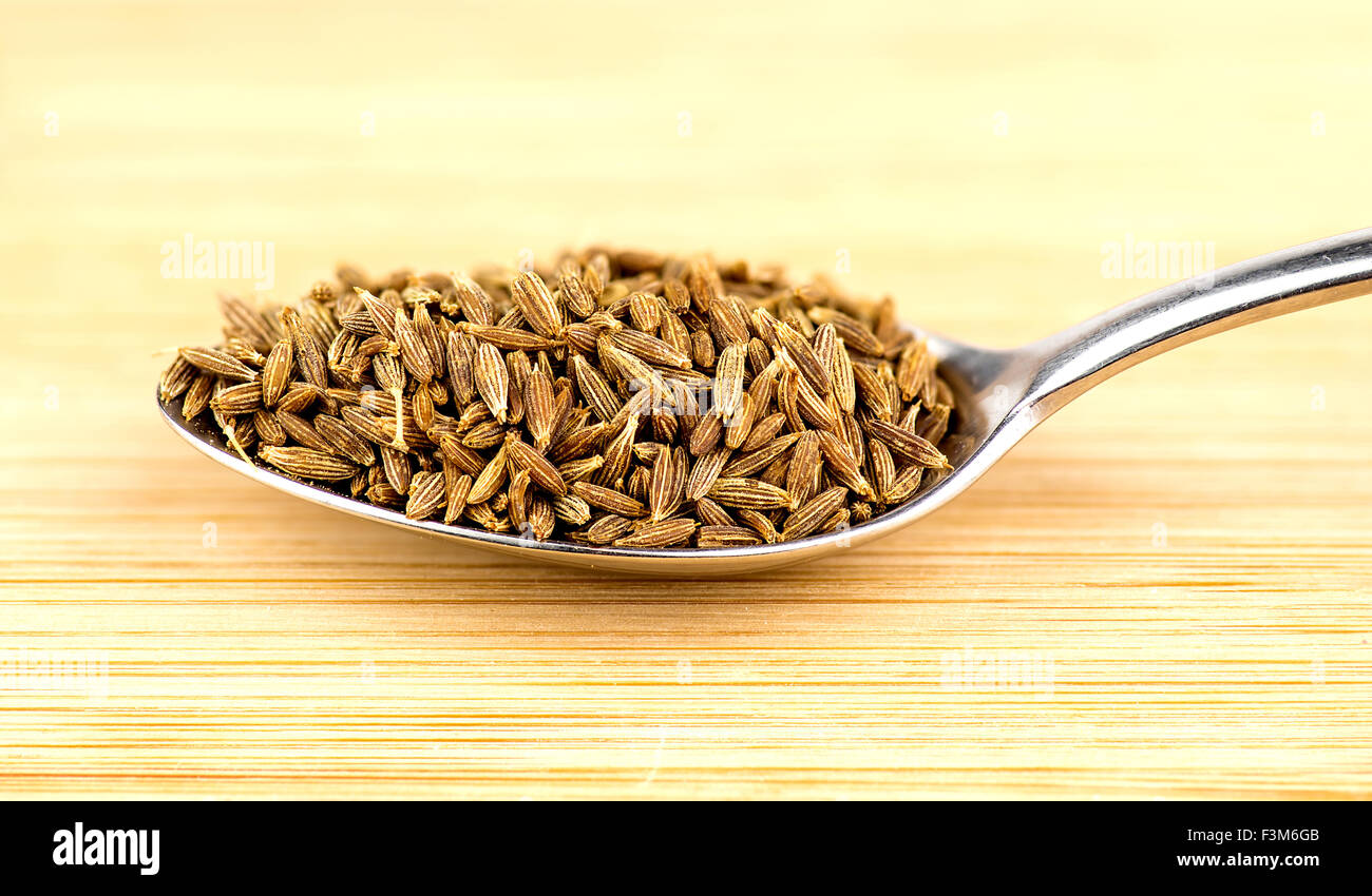 Spoonful of cumin seeds against wooden background Stock Photo