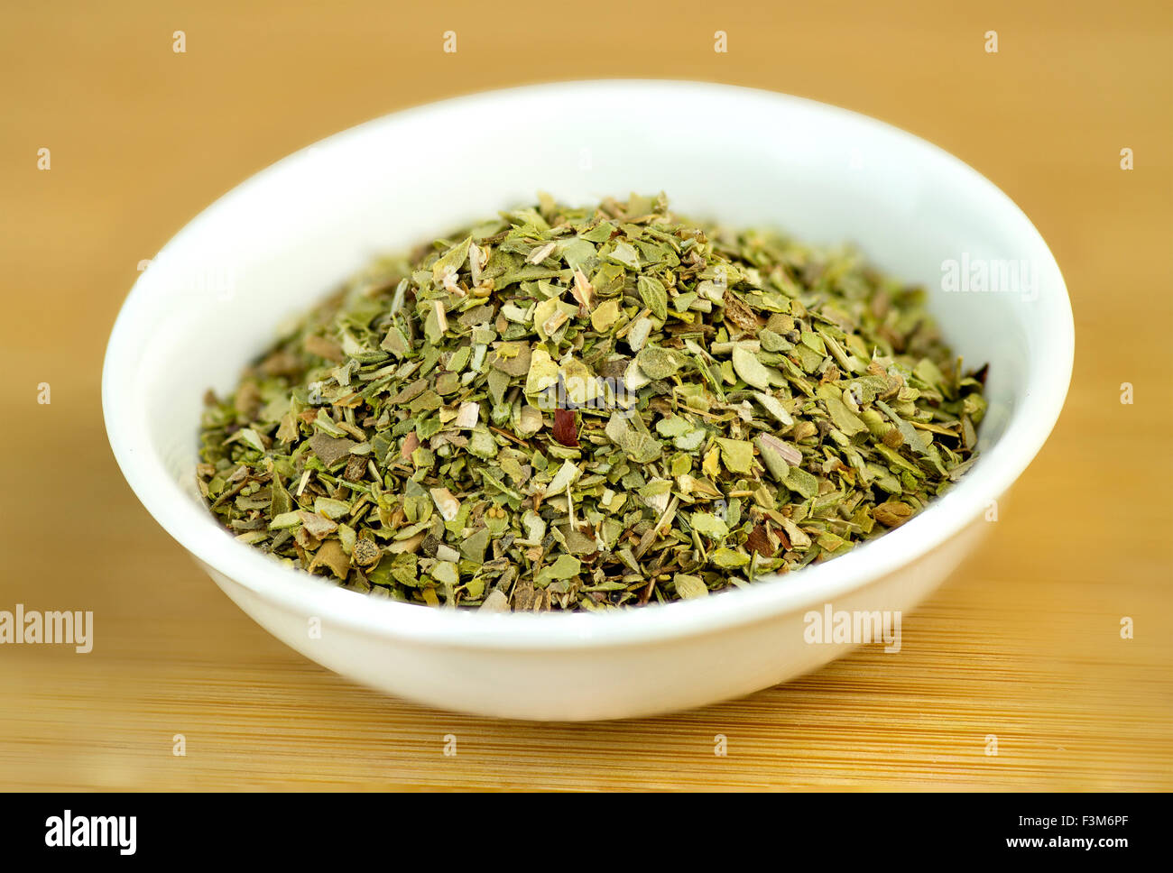 Dehydrated oregano macro in white bowl on wooden background Stock Photo