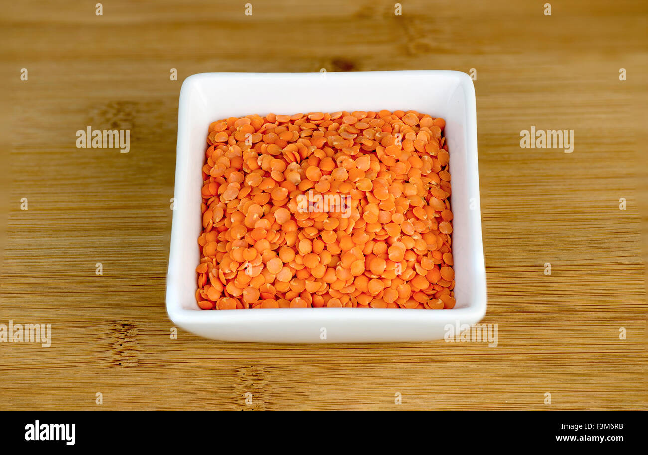 Macro of red split lentils in white bowl on wooden board Stock Photo