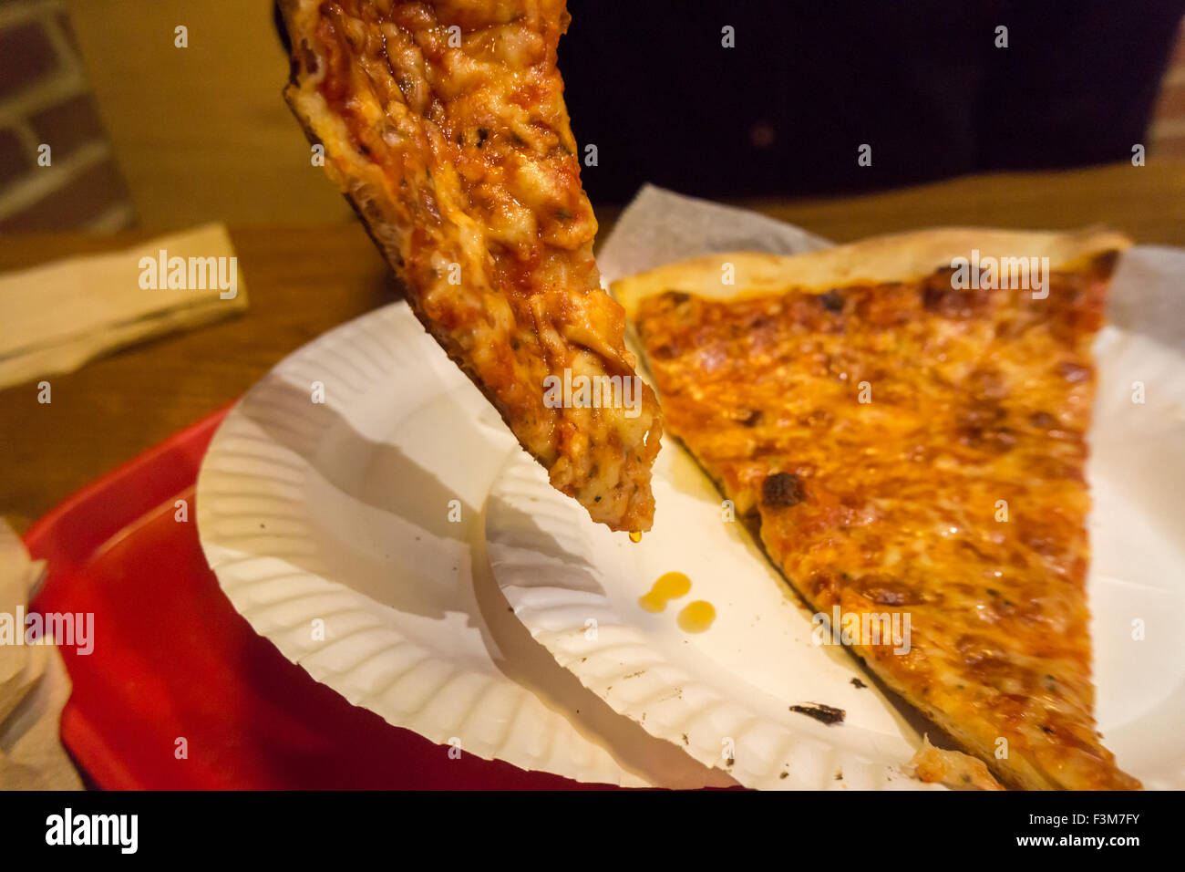 A hungry consumer drains her slice of pizza to remove the excess grease in a pizzeria in New York on Friday, October 2, 2015. A recent study reveals that degreasing your slice removes up to 76 calories and 4 1/2 grams of fat, or up to two pounds on your waistline every year. The average American eats 23 pounds of pizza yearly. (© Richard B. Levine) Stock Photo
