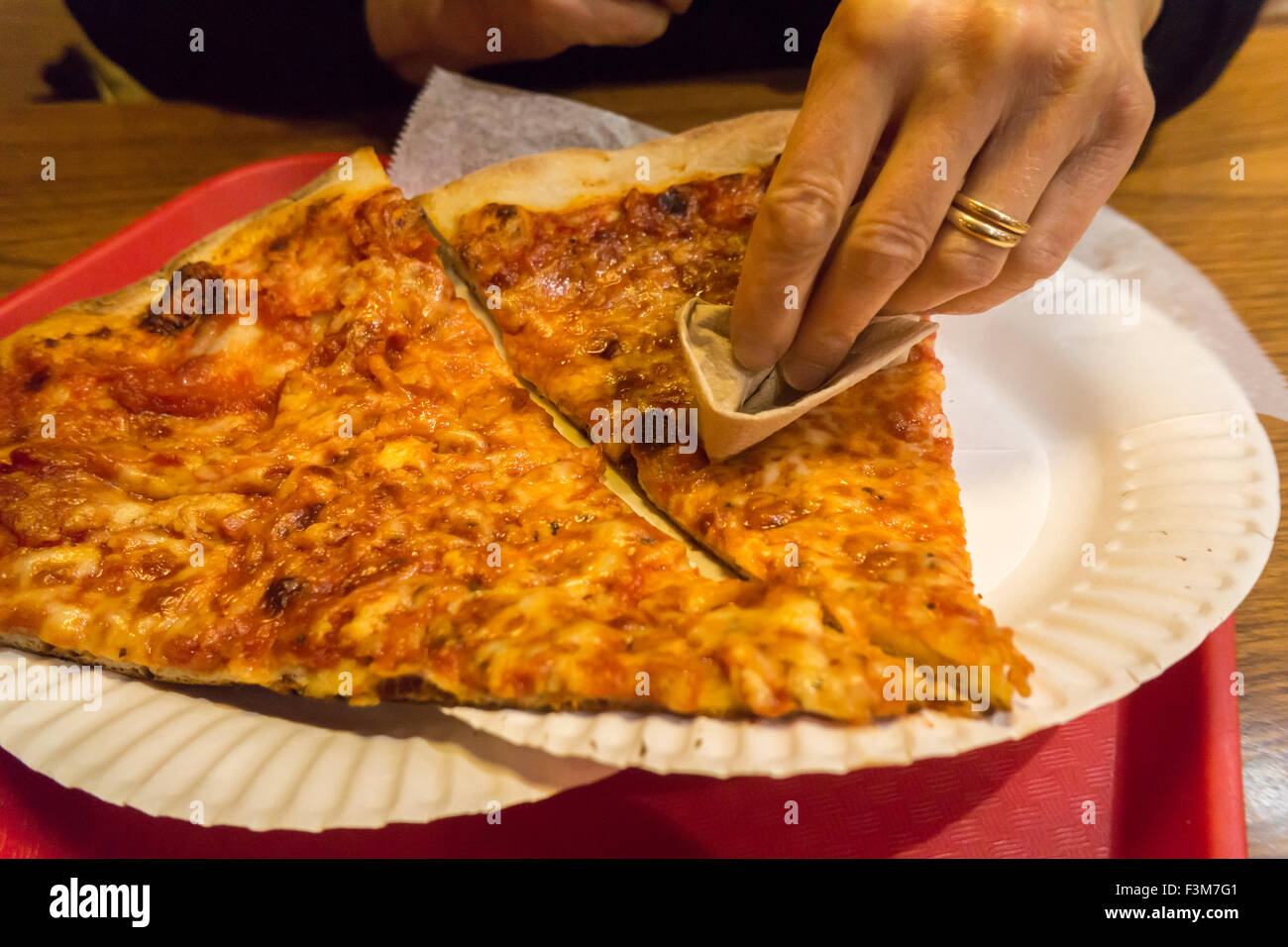 A hungry consumer dabs her slice of pizza with a napkin to absorb the excess grease in a pizzeria in New York on Friday, October 2, 2015. A recent study reveals that degreasing your slice removes up to 76 calories and 4 1/2 grams of fat, or up to two pounds on your waistline every year. The average American eats 23 pounds of pizza yearly. (© Richard B. Levine) Stock Photo