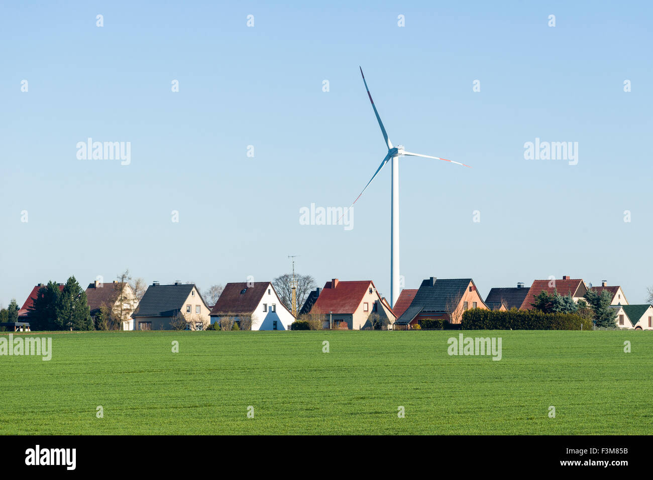 A wind power plant behind village houses in agricultural landscape Stock Photo