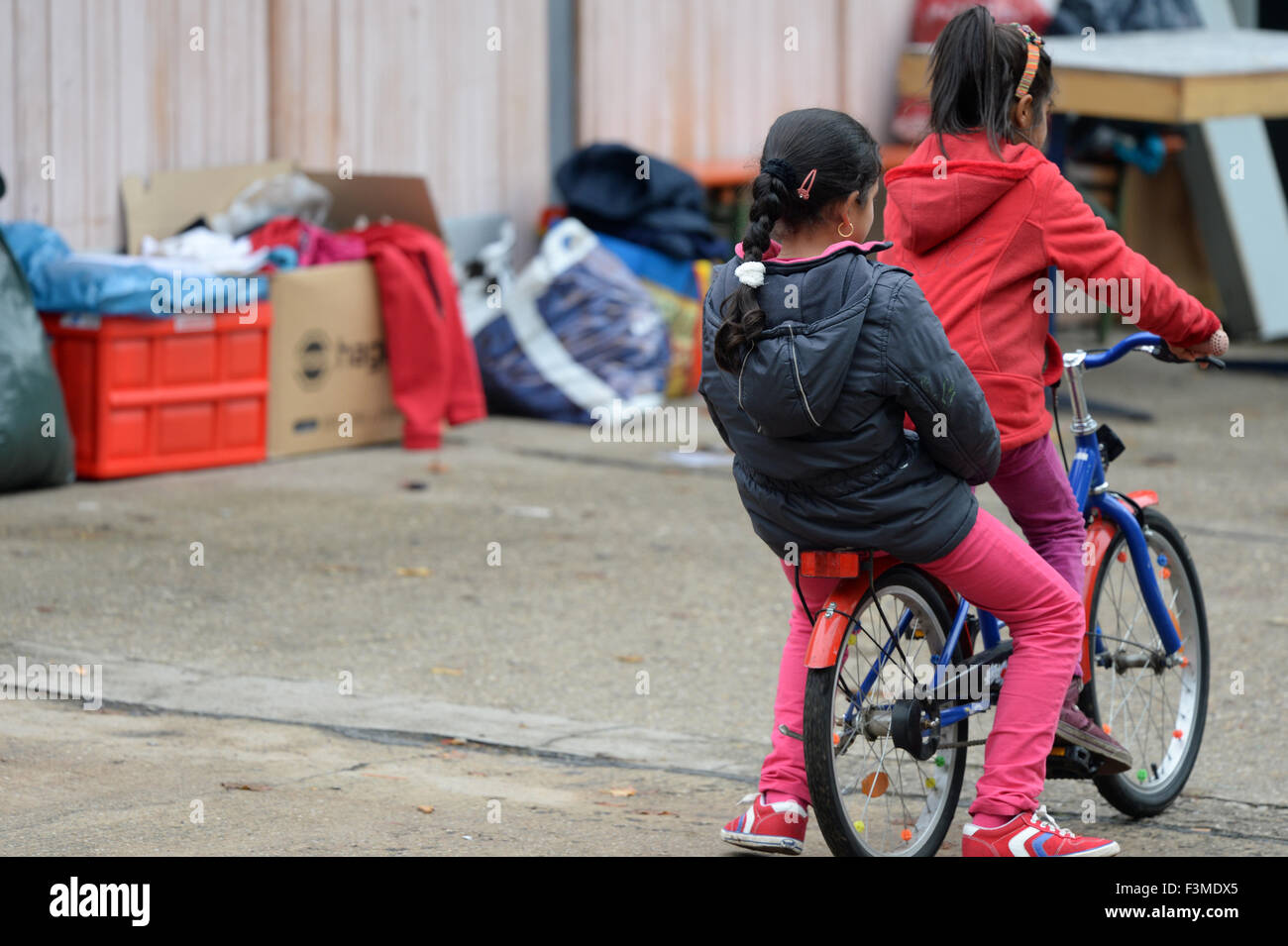 Potsdam, Germany. 9th Oct, 2015. Two refugee girls ride a bicycle on the grounds of a refugee processing centre in the public authorities headquaters in Potsdam, Germany, 9 October 2015. The German state of Brandenburg will be accepting more than 40,000 refugees after the orders of the Interior Minister. Photo: RALF HIRSCHBERGER/dpa/Alamy Live News Stock Photo