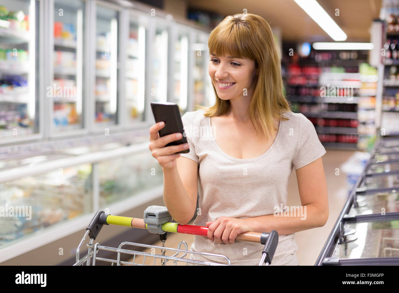 Cute young woman texting on her cell phone in supermarket. Stock Photo