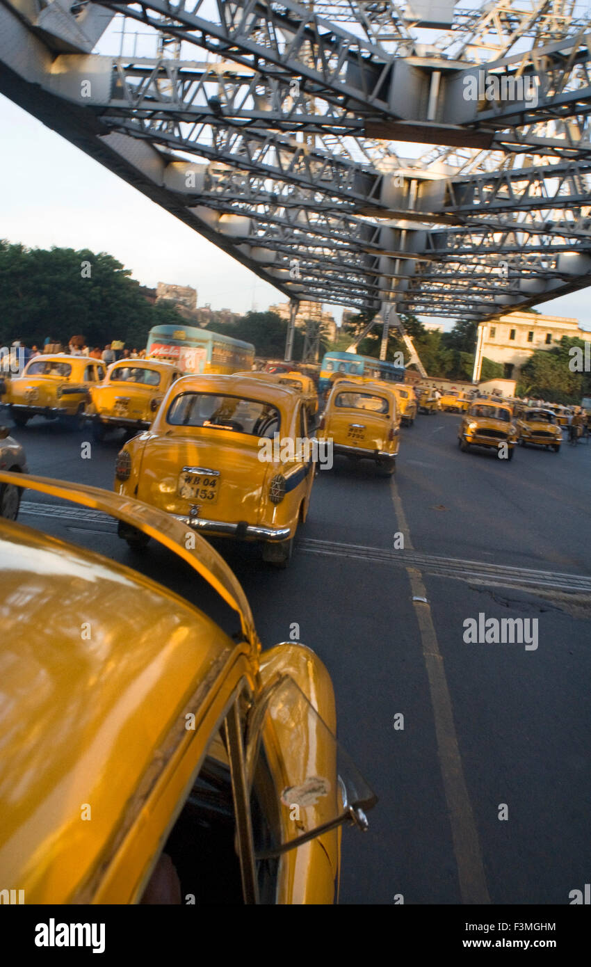 Yellow Ambassador taxis (cabs) crossing Howrah Bridge in Kokata (Calcutta), India. Kolkata, West Bengal, India. The taxi is one Stock Photo