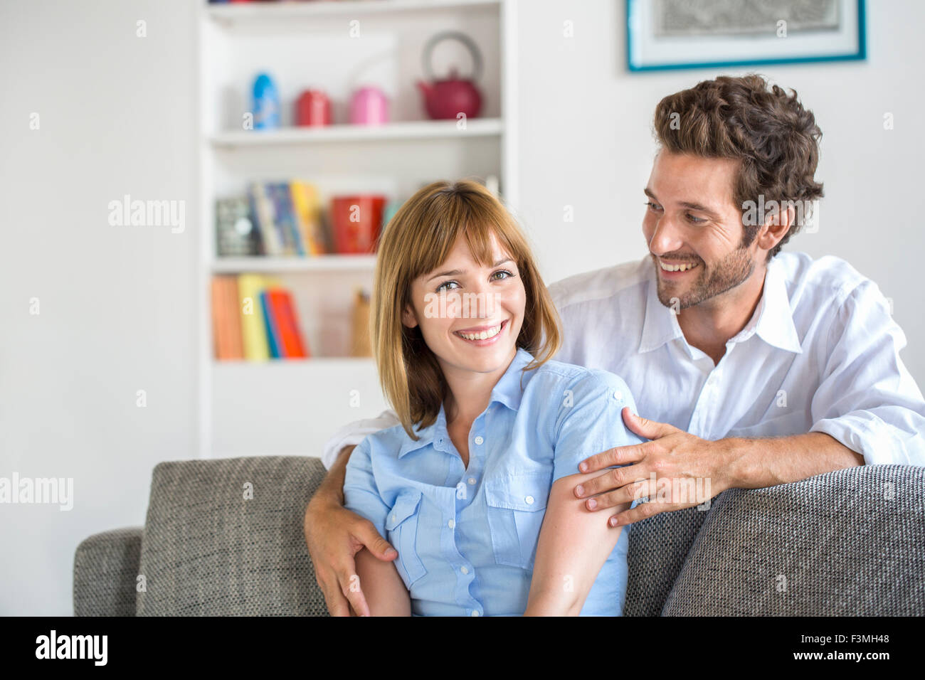 Portrait of cheerful thirty year old couple sitting on sofa in modern white apartment Stock Photo