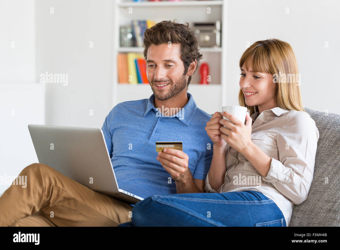 Mid adult couple shopping using laptop and credit card in modern apartment. Ecommerce Stock Photo