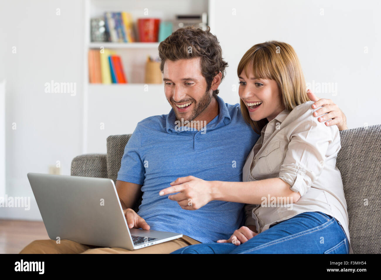 Happy success young couple with laptop on sofa in modern white apartment. Stock Photo