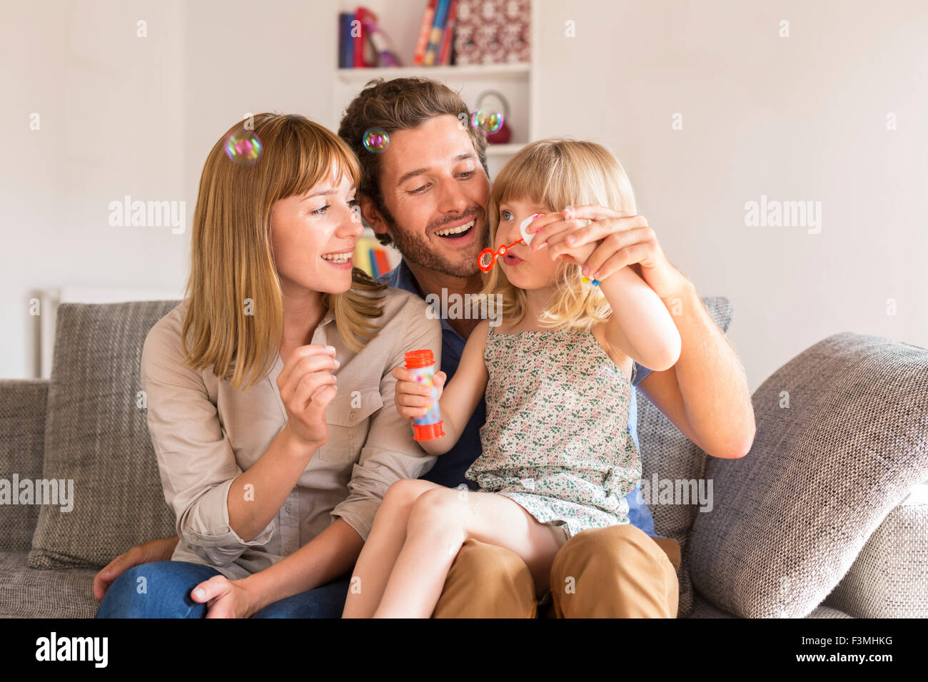 Cheerful parents and daughter blowing bubbles in white modern house Stock Photo