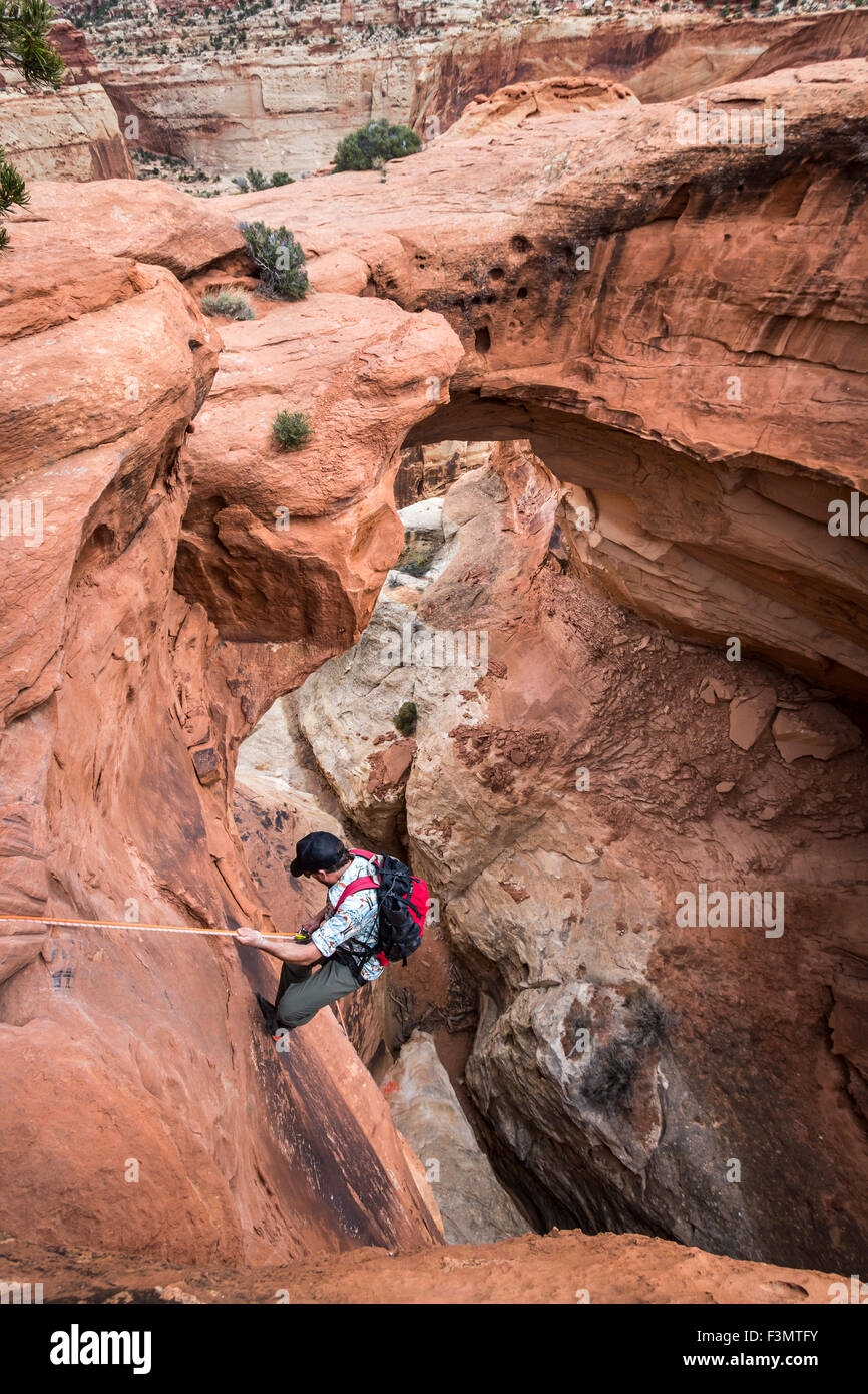 A man rappels down into a canyon below a natural rock arch in the desert. Stock Photo