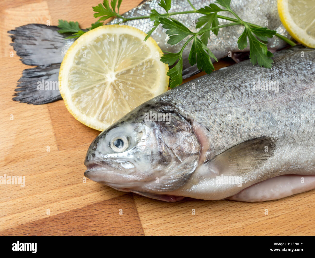 Two raw rainbow trouts on wooden board decorated with parsley and lemon slices Stock Photo