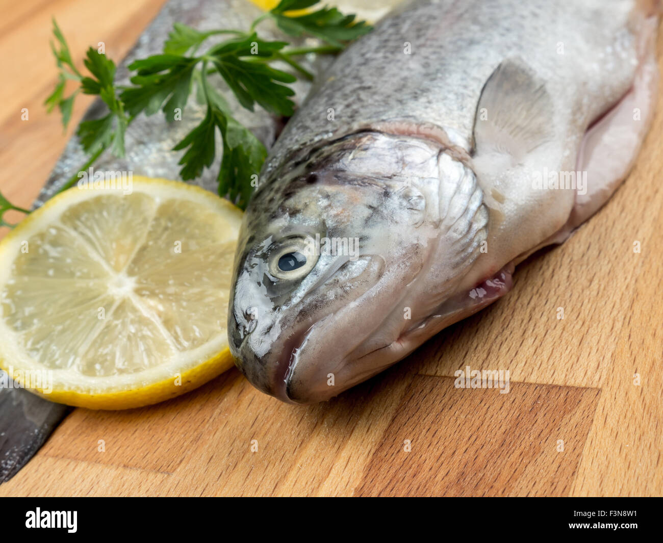 Two raw rainbow trouts on wooden board decorated with parsley and lemon slices Stock Photo