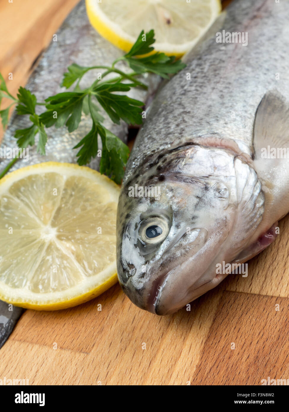 Two raw rainbow trouts on wooden board decorated with parsley and lemon slices Stock Photo