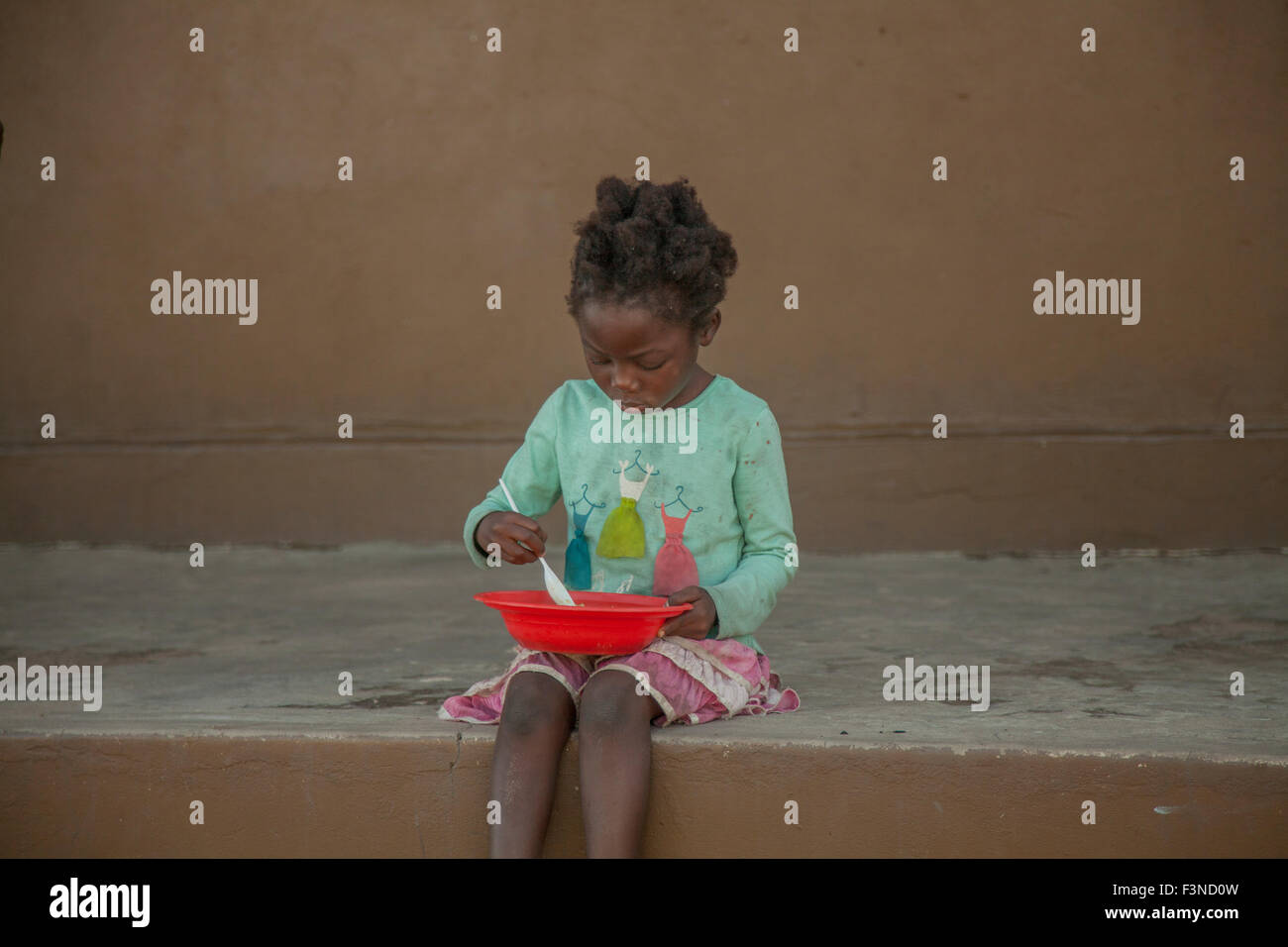 African girl sitting wile eating food given by malnutrition program. Stock Photo