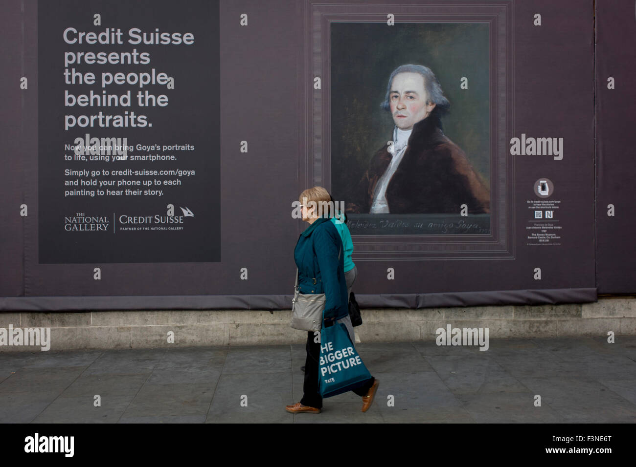 a woman walks with a Tate Modern gallery bag walks past a Goya portrait, sponsored by Credit Suisse and advertised on a construction hoarding outside the National Portrait Gallery. Stock Photo