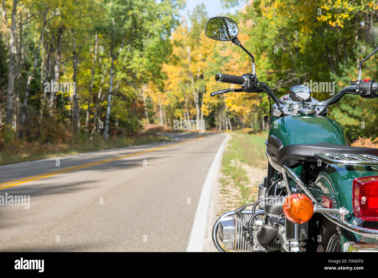 A green motorcycle alongside a curving open road in the Fall.  Selective focus on motorcycle with copy space in left frame. Stock Photo