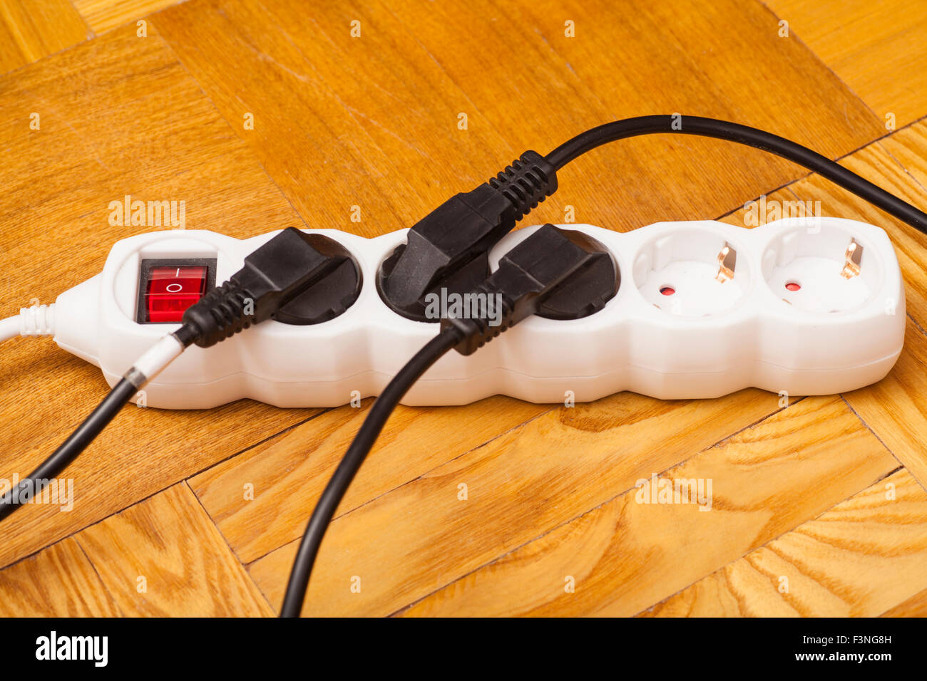 Many plugs plugged into electric power bar on floor Stock Photo