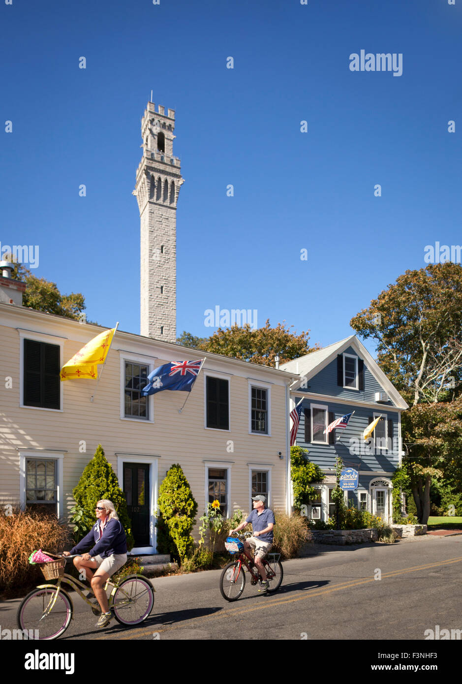 Couple biking in front of Gabriel's Bed and Breakfast with Pilgrim Monument in background, Provincetown, Massachusetts , USA Stock Photo