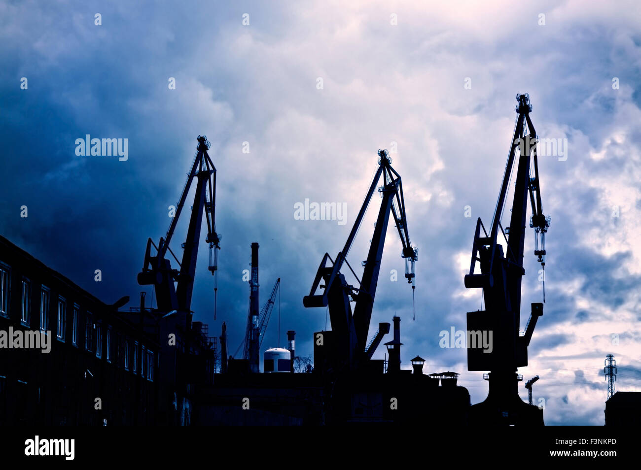 Industrial conceptual image. Dark and sullen clouds over industrial shipyard area with cranes. Stock Photo