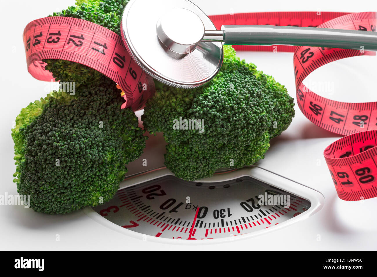 Diet healthy eating weight control concept. Closeup green broccoli with measuring tape and stethoscope on white scales Stock Photo