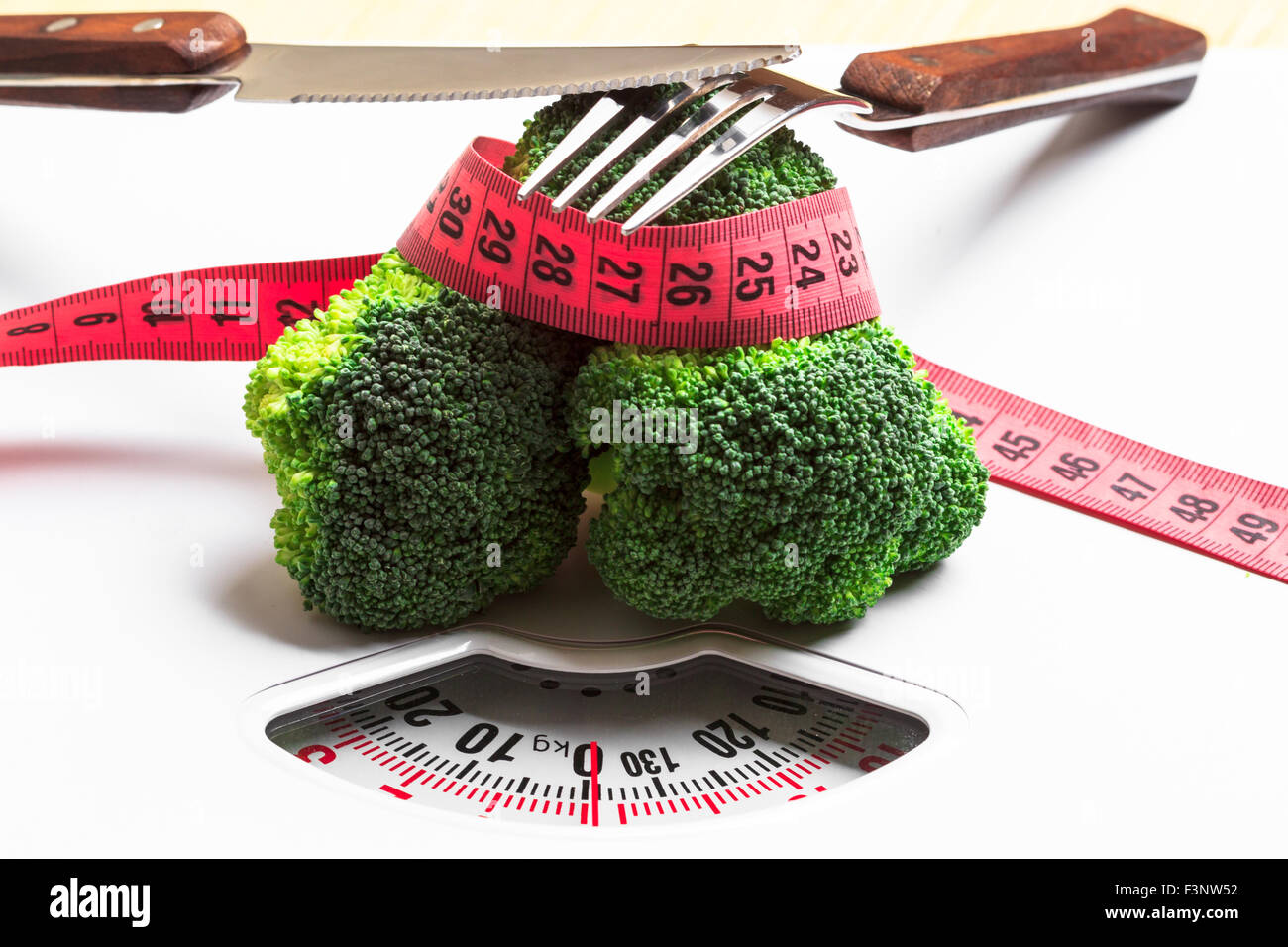 Diet healthy eating weight control concept. Closeup green broccoli measuring tape and fork knife on white scales Stock Photo