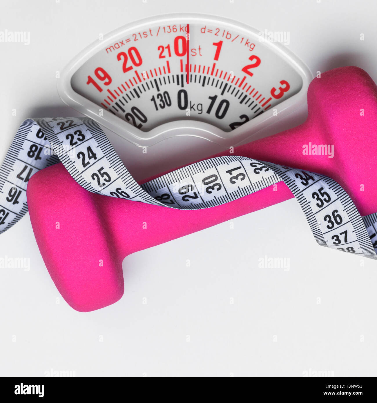 Measure tape with dumbbells and weight scale on the pink