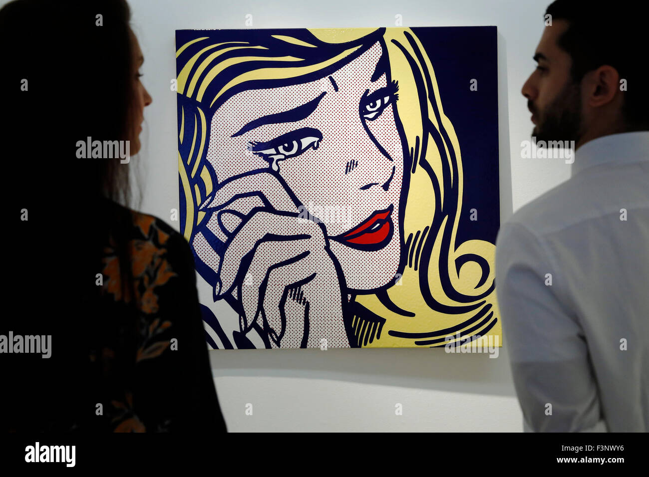 Christie's employees pose with artist Roy Lichtenstein's artwork ' Crying Girl' (R) at Christie's Auction House in London, UK Friday October 9, 2015.   It is expected to achieve US $9million dollars when it comes to auction in New York in November.  They will be on dispay in the UK during Frieze Art Fair week until October 17. Stock Photo