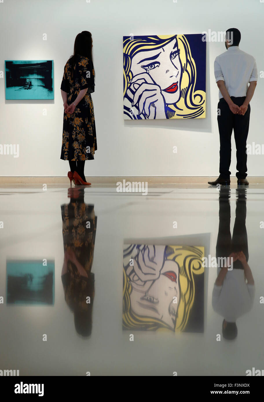 Christie's employees pose with artist Roy Lichtenstein's artwork ' Crying Girl' (R) and Andy Warhol's 'Little Electric Chair' at Christie's Auction House in London, UK Friday October 9, 2015.  They are both expected to achieve US $9million dollars when they come to auction in NNew York in November..  They will be on dispay in the UK during Frieze Art Fair week until October 17. Stock Photo